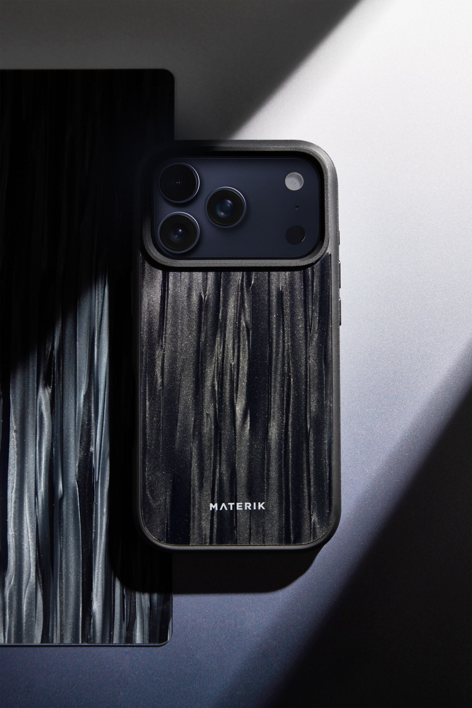 Materik PureCase for iPhone 17 Pro in black, flat-lay with dramatic light and shadow