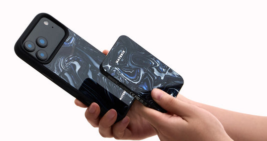 Hands holding an iPhone in a black marbled Materik case while attaching a MagSafe accessory to the back